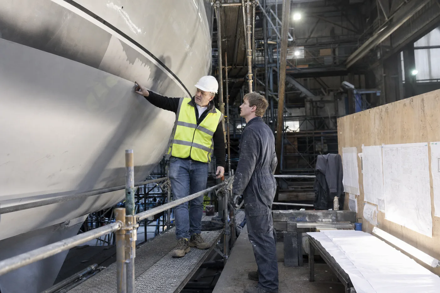 A project manager reviewing work beside a yacht under scaffolding
